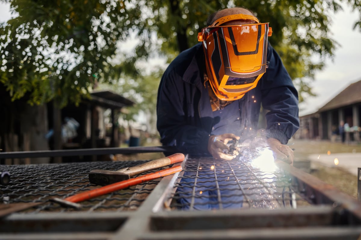 Worker wearing a protective mask and gloves, performing manual welding on metal outdoors